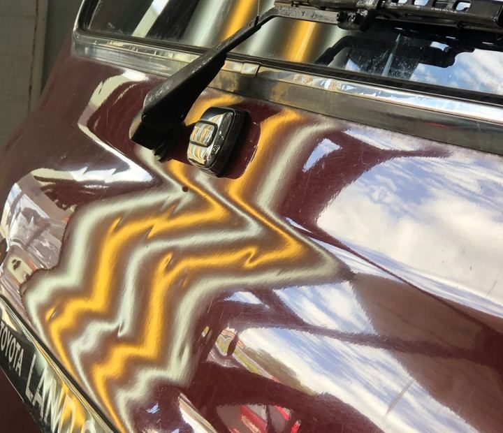 A technician's striped PDR light reflecting in the panel of a LandCruiser during a dent repair